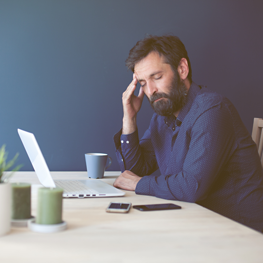 Man rubbing head in front of open laptop