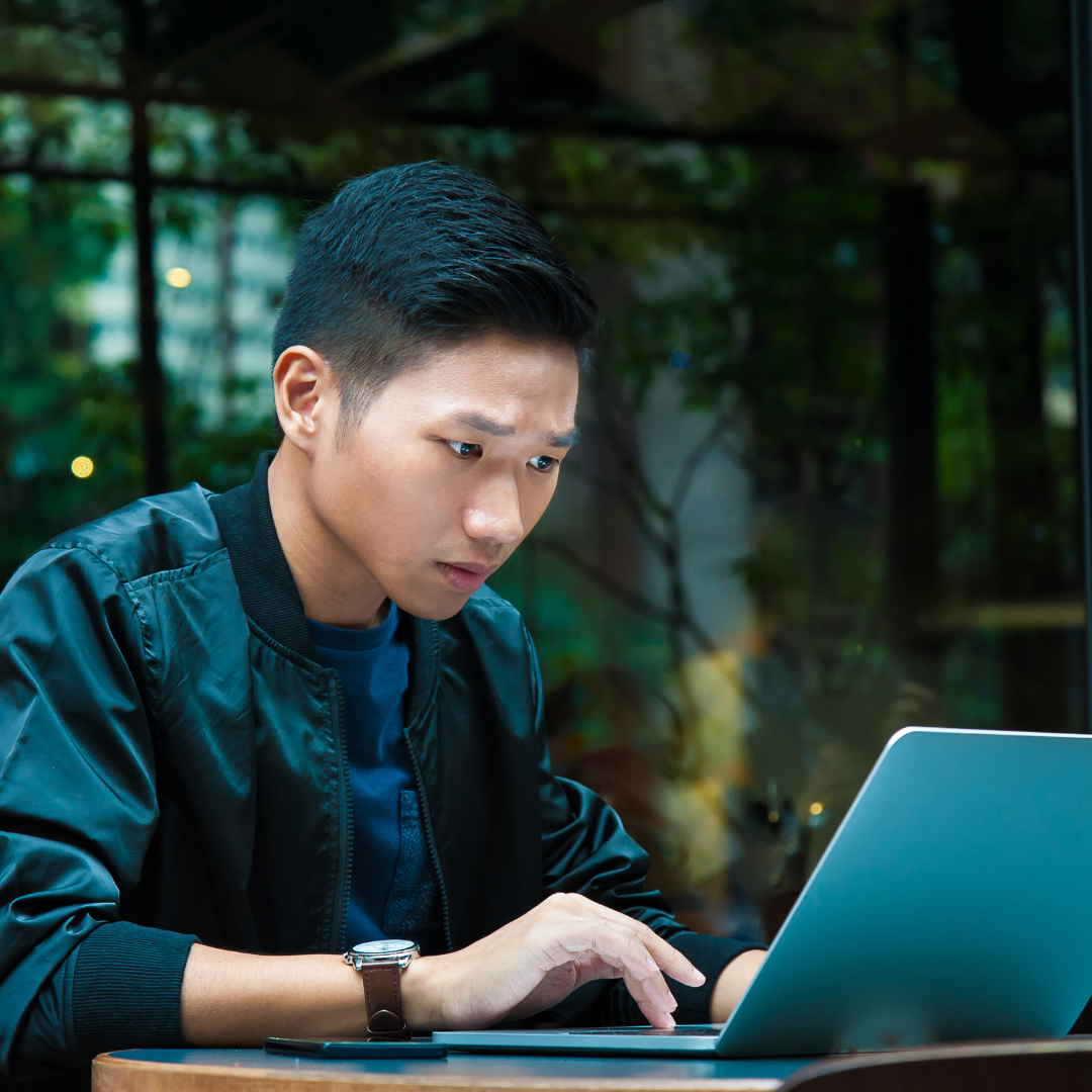 Asian man, in casual clothing, looking intently at laptop screen